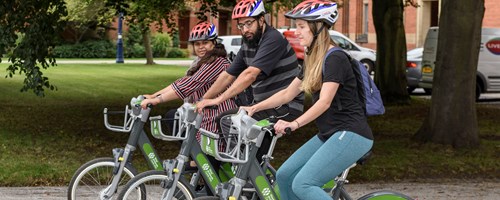 Three people lined up riding their bikes through park, wearing helmet gear