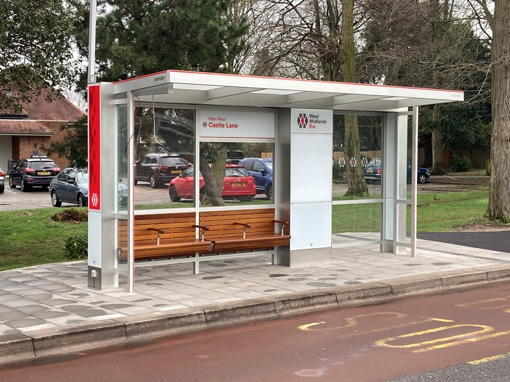 Modern West Midlands bus shelter at Castle Lane with seating, glass panels, and red and white branding.