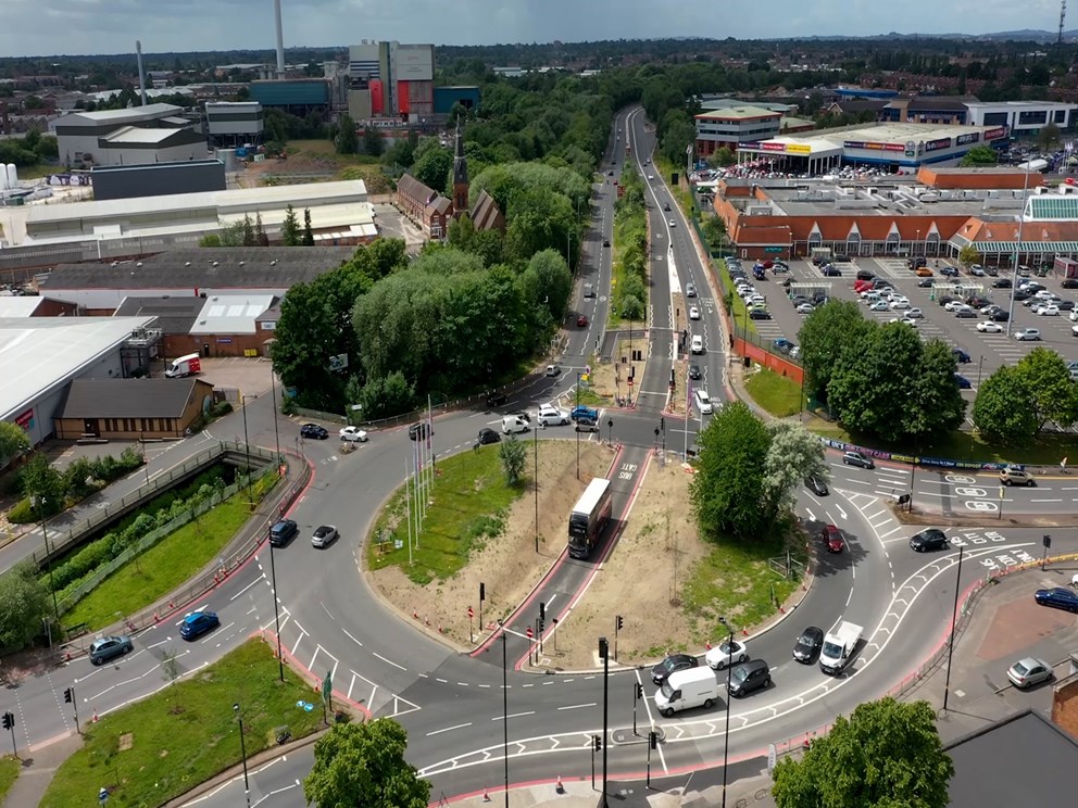 Aerial view of a busy roundabout with new bus lanes, cycle paths, and traffic near shops and housing.