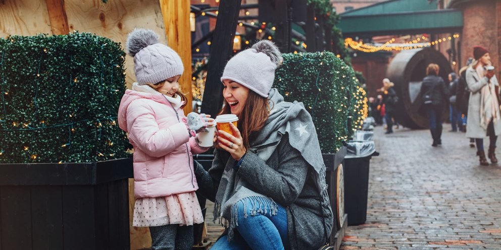 A mother and daughter enjoying hot drinks at a Christmas market.